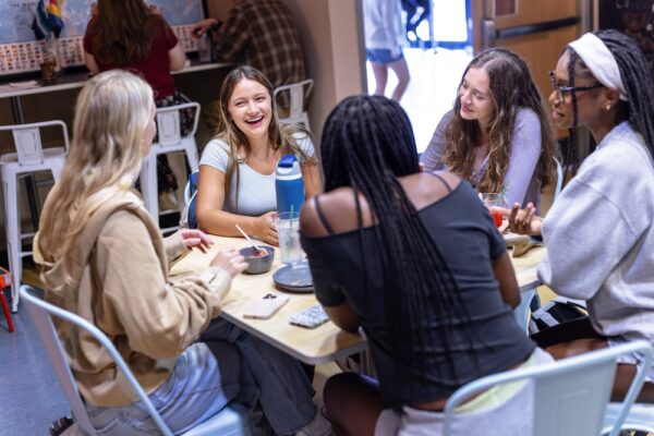 Allegheny College students sit at a table in a dining hall and talk to one another.