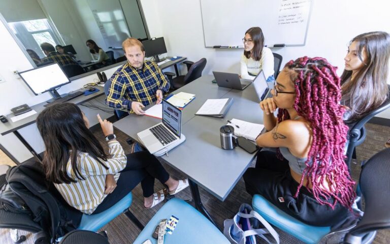 professor and students sitting around a small meeting table in discussion