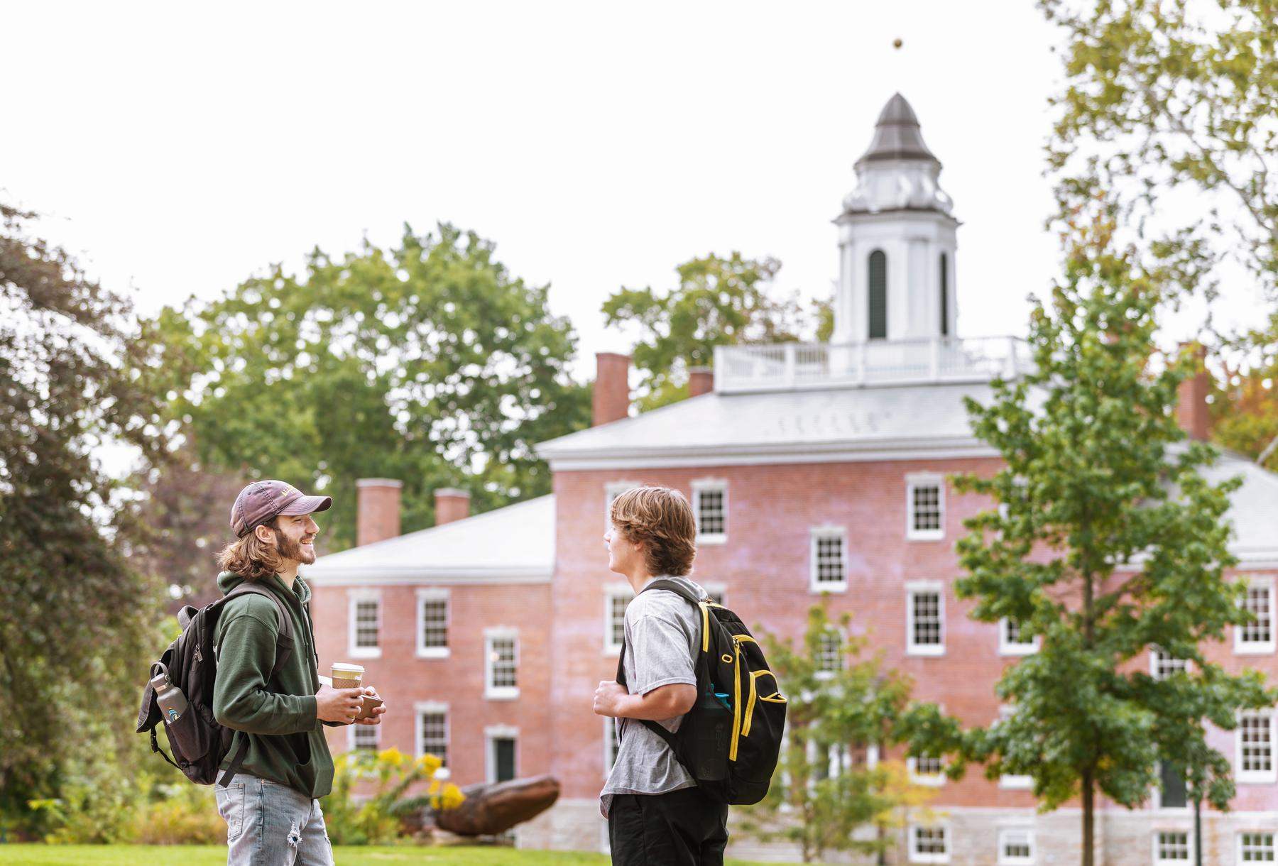 a group of students standing in a grassy area in front of a red brick building