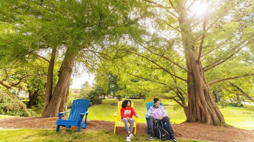 two students sitting in chairs in wooded area