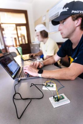 two students at laptops, one has arduino chip sets connected to their computer