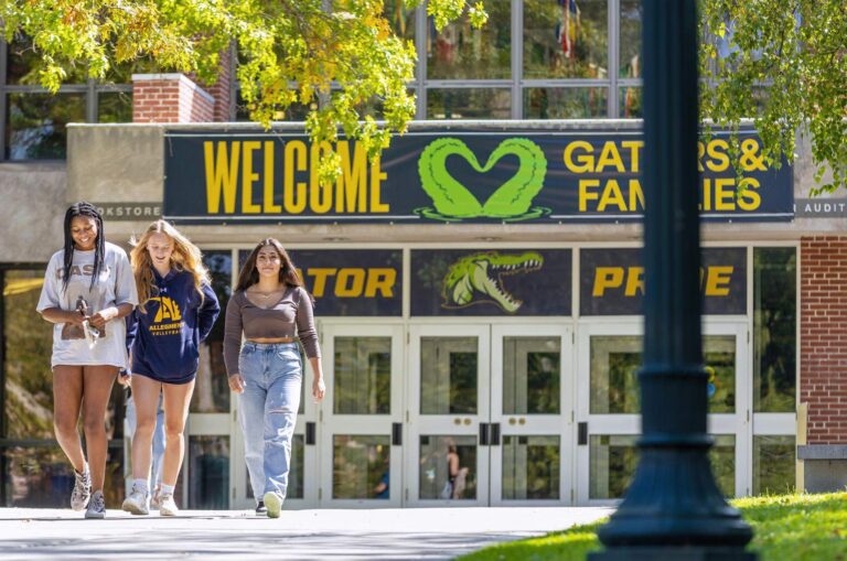 Three female students walking on campus below a sign welcoming Gators and families.