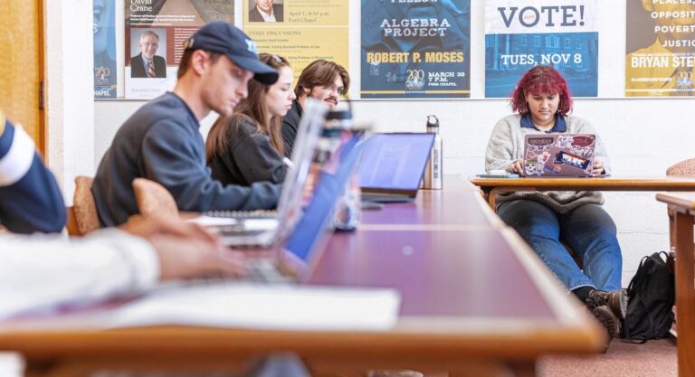 a group of students sitting at tables looking at laptops