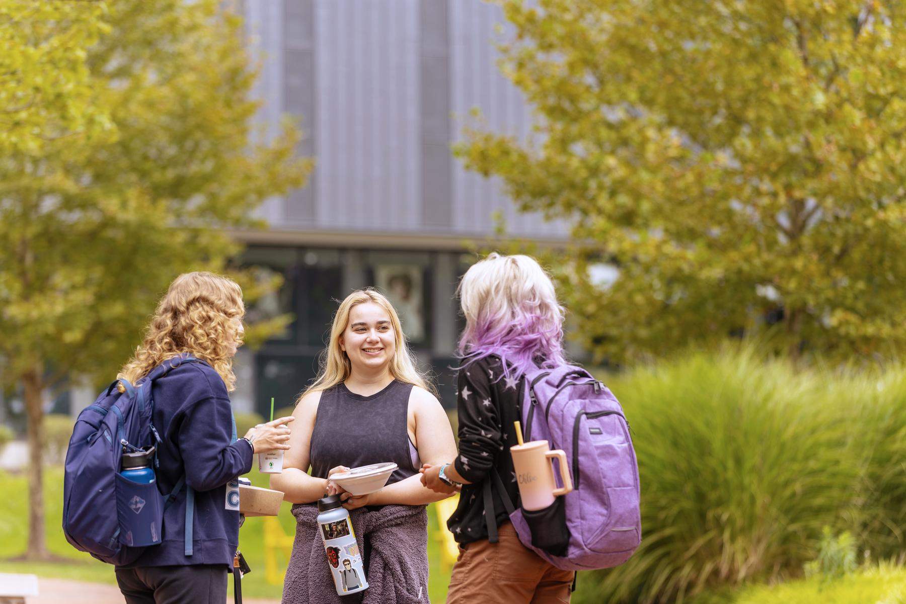 a group of students talking to each other in front of a gray building