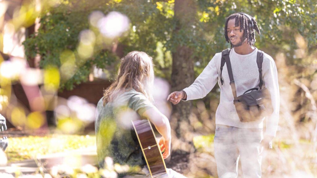 a student talking to another student who is playing the guitar