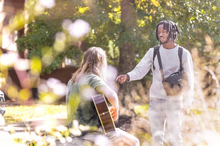 a student talking to another student who is playing the guitar