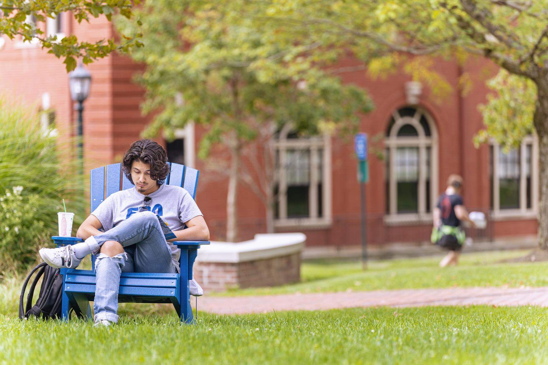 a person sitting on a blue bench in the grass in front of a red brick building