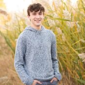 a man in a gray sweater standing in front of tall grass