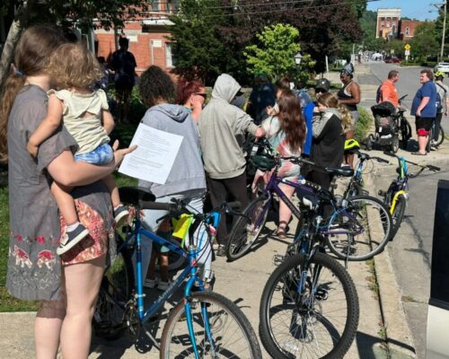 A group of people stand on a sidewalk with bikes.