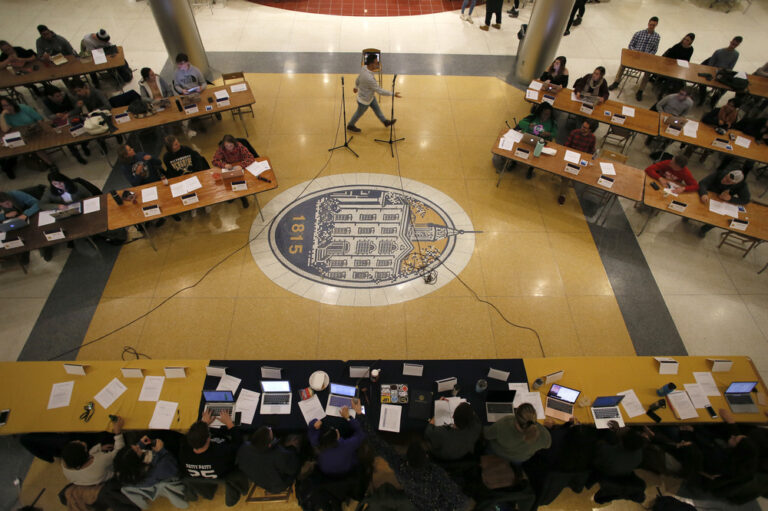 students sitting at rows of tables with computers and papers in front of them