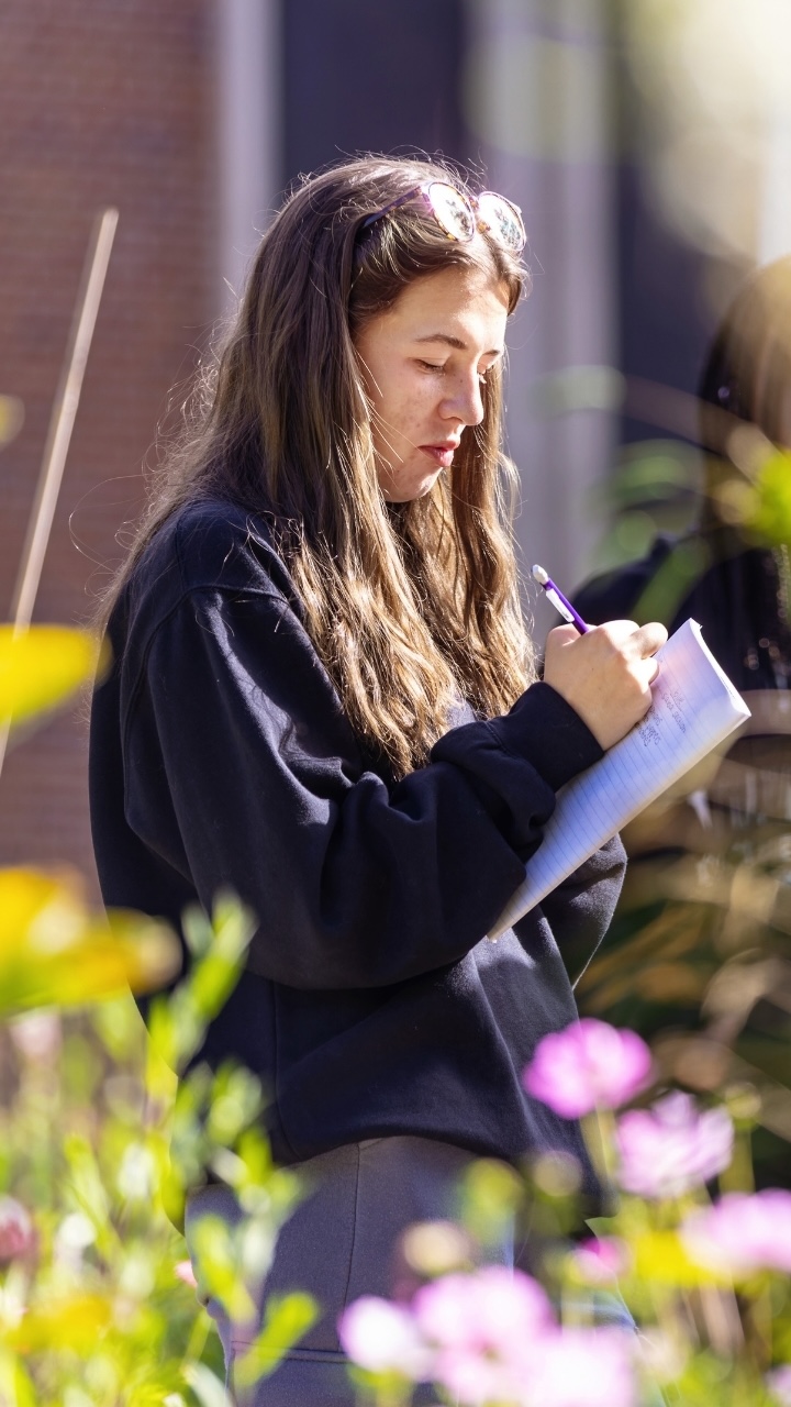 A student writes in a notebook in a community garden at Allegheny College