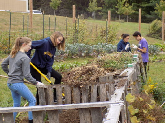 Students shoveling dirt in a garden setting for Service Saturday.