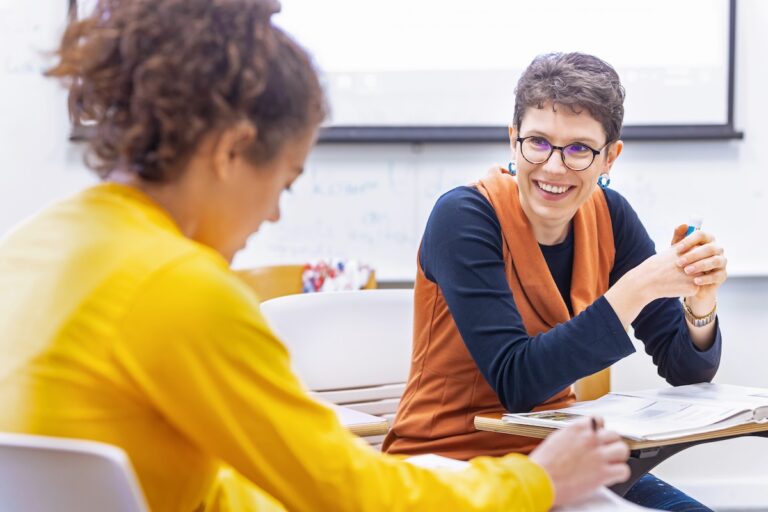 An Allegheny College Professor sits at a desk and listens to a student talking