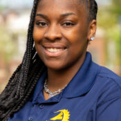 Woman with long black braids parted to the side wearing a navy blue collared shirt