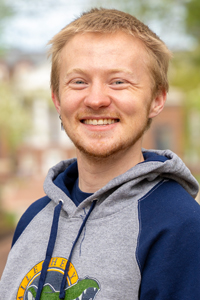 Man with short blonde hair wearing a gray and navy blue hooded sweatshirt