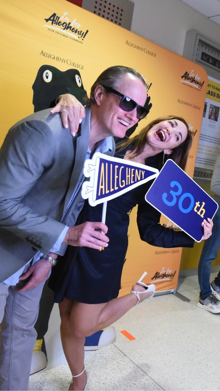 Two people hold up Allegheny College signs while posing for a photo booth