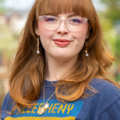 Woman with red hair and clear rimmed glasses wearing an Allegheny shirt