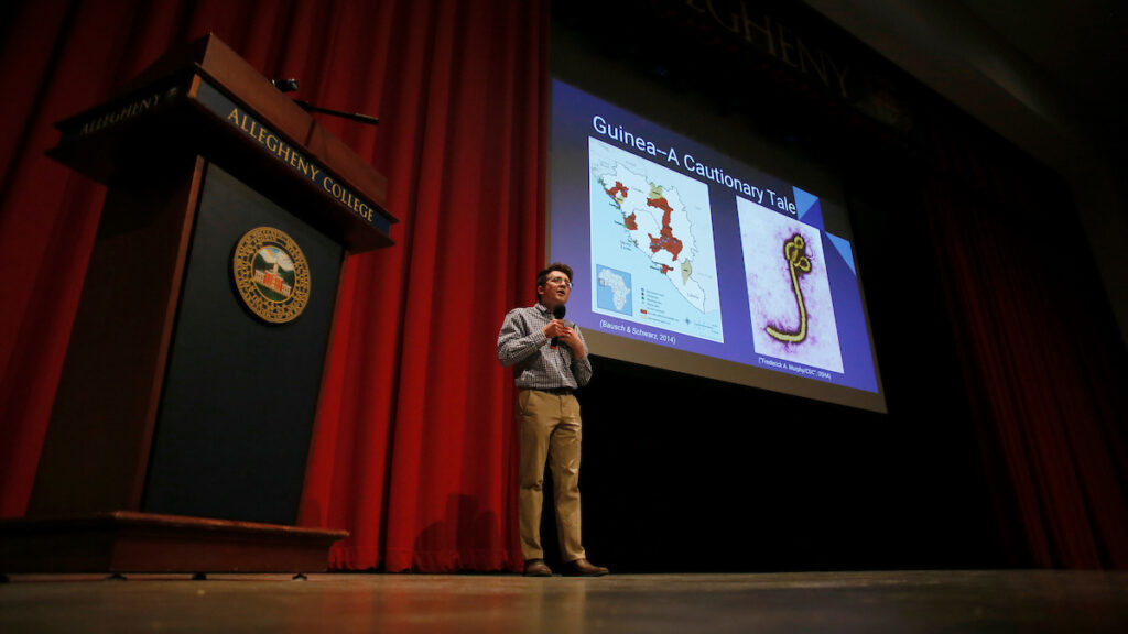 a person standing in front of a podium against a red curtain