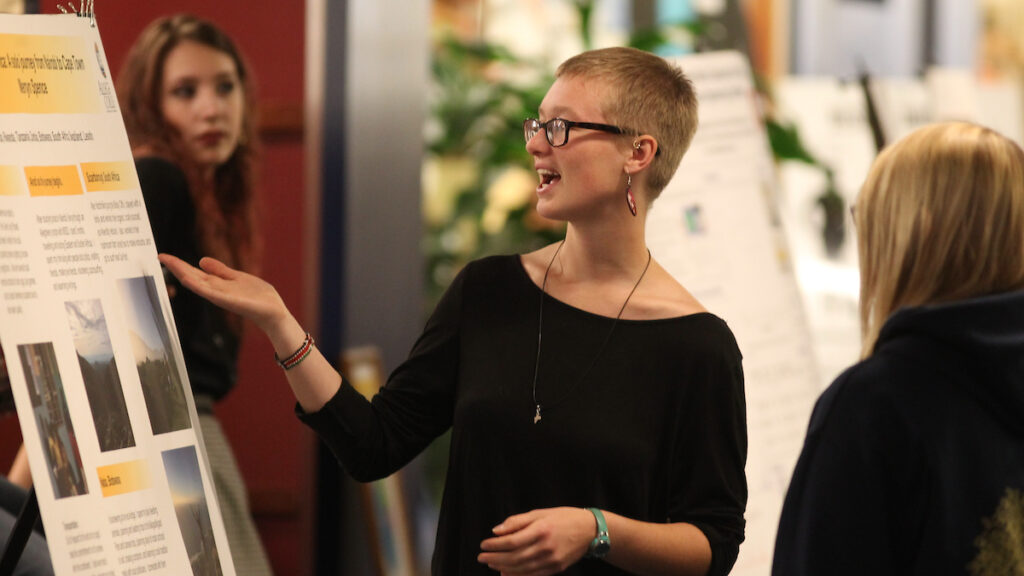 a person with glasses in a black shirt gesturing to her left