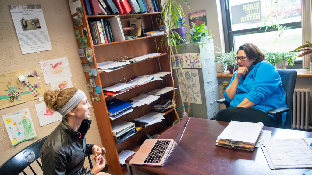 people sitting at a desk in an office with a bookshelf between them
