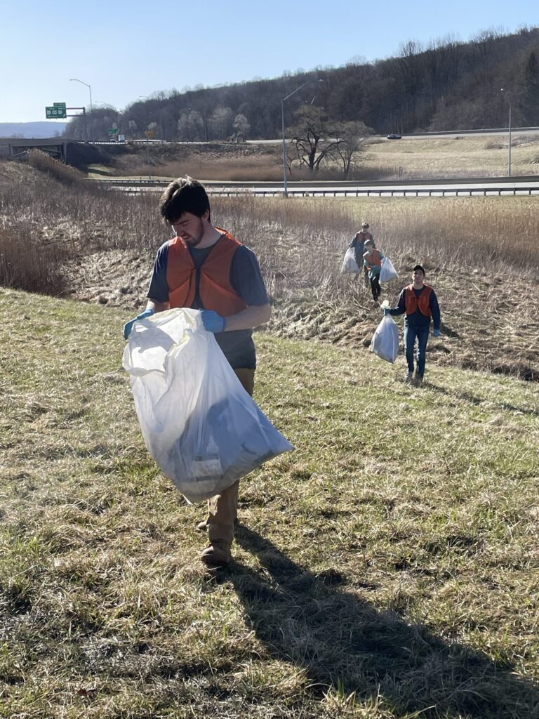 a group of students wearing vests carrying garbage bags while they walk across a grassy field