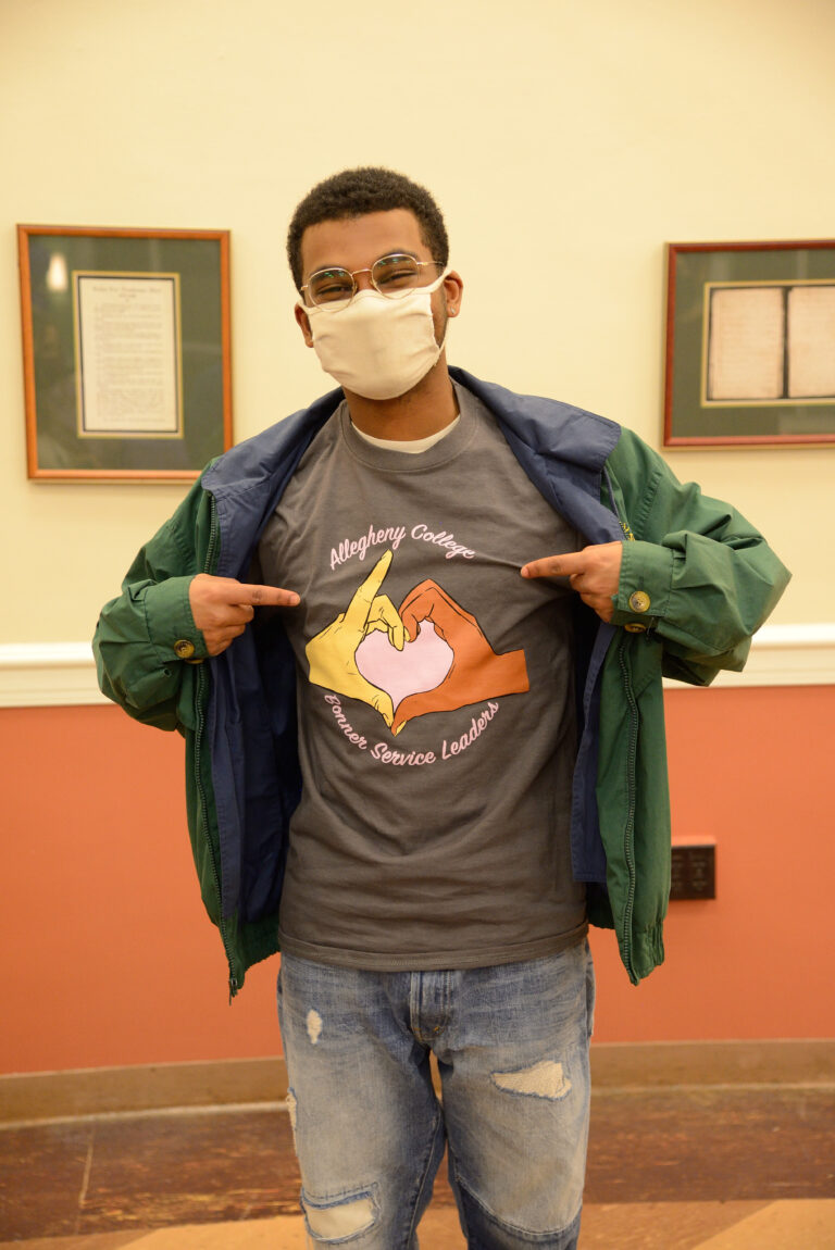 a student wearing a mask and pointing at his shirt