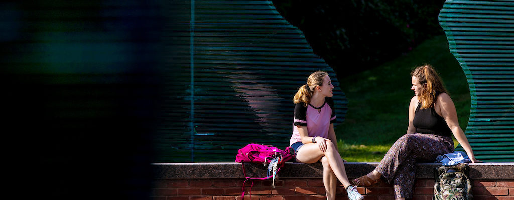 two women sitting on a ledge talking to each other