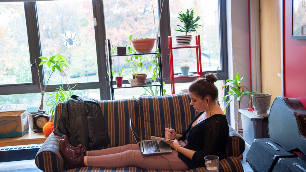 a student sitting on a couch with a laptop in front of a window