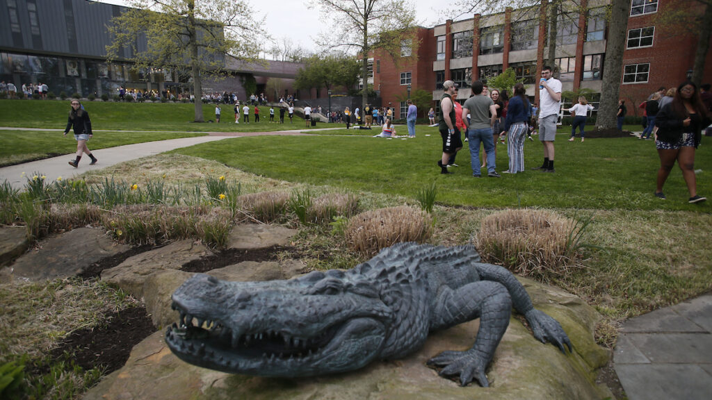 a statue of a crocodile on a rock with students standing in the background