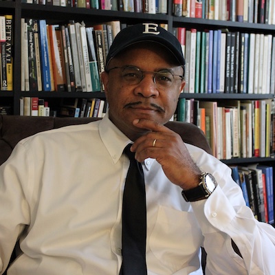 portrait of a person in a white shirt and tie in front of a bookshelf