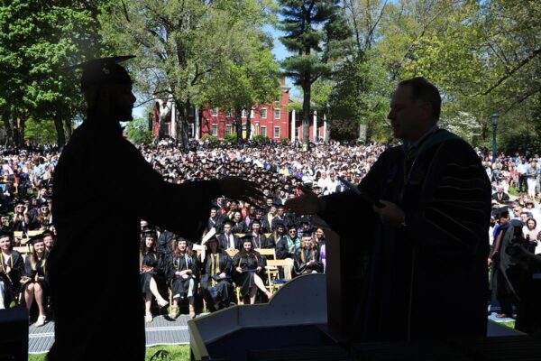 a silhouette of a student receiving a degree on stage in front of a large crowd