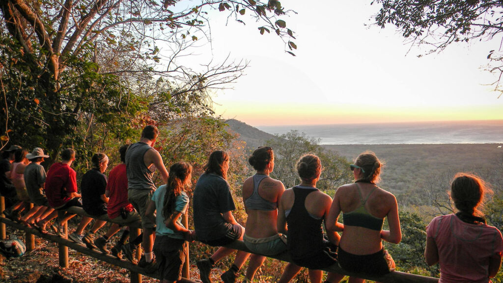students sitting on a fence overlooking a sunset