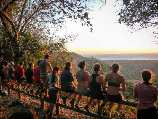 students sitting on a fence overlooking a sunset