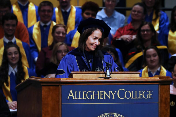 a person in blue gown and cap speaking at a podium