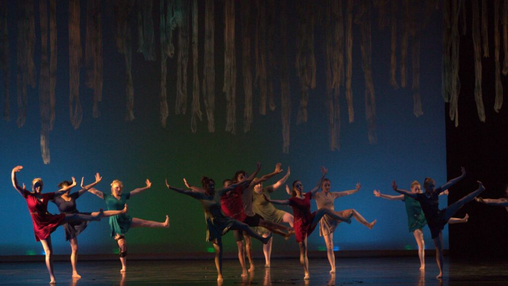 a group of students dancing on a dark, dimly lit stage