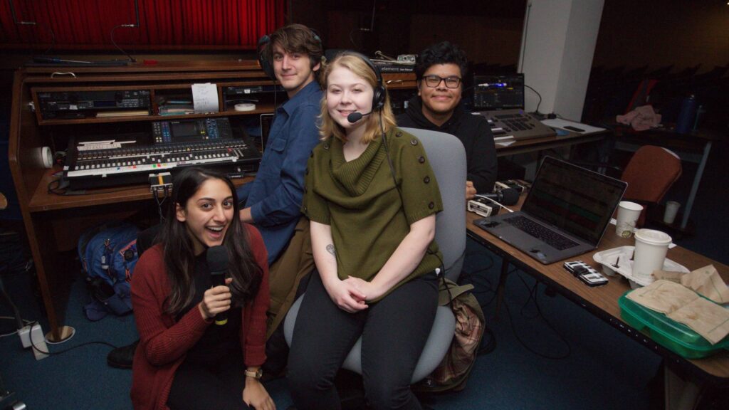 a group of four students sitting in a room surrounded by audio equipment