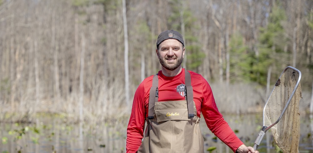 Allegheny College Professor Matthew Venesky stands in a marsh holding a net